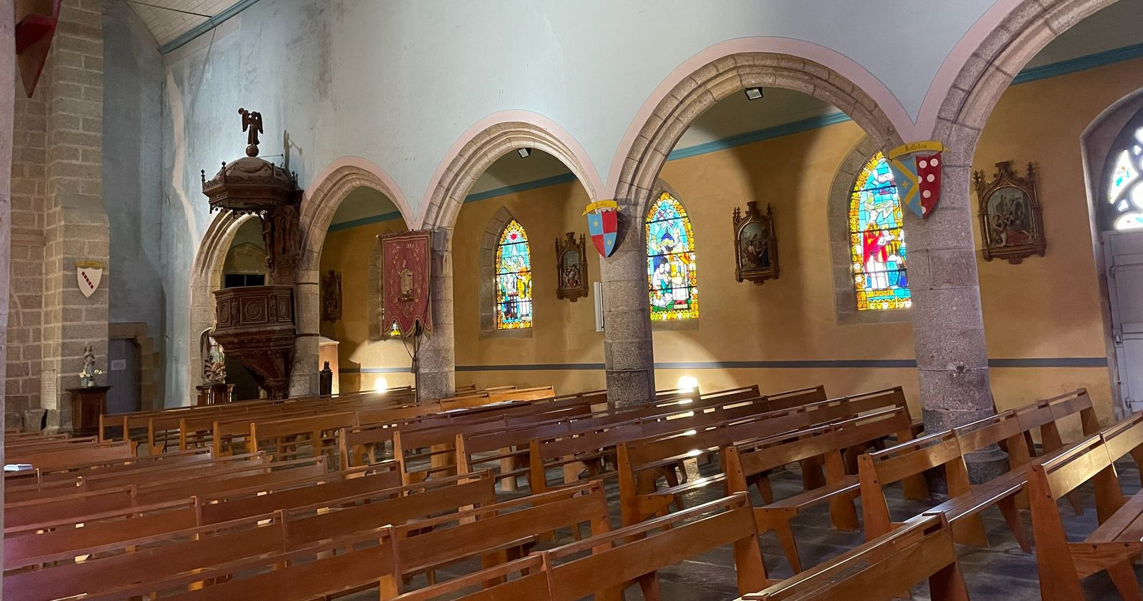 Nave of a Catholic church with wooden pews, stone arches and stained glass windows
